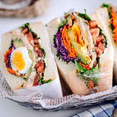 three sandwiches with meat, lettuce and an egg on top in a basket