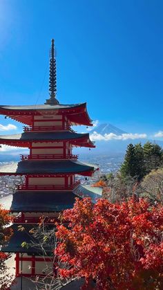 a tall red and white pagoda sitting on top of a lush green hillside under a blue sky