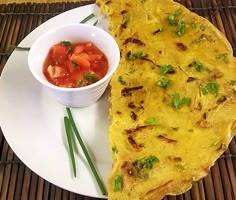 an omelet on a plate with a small bowl of tomato sauce next to it