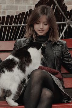 a woman sitting on a red bench with her cat next to her, she is petting the cat