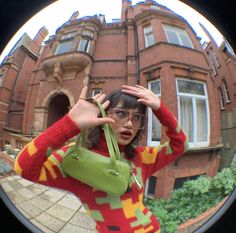 a woman is taking a selfie in front of a building with a green purse