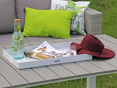 a tray with drinks and a hat on top of a patio table next to pillows