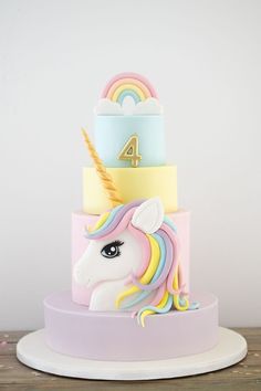 a multi - tiered cake with a unicorn on the front and rainbow decorations on the back