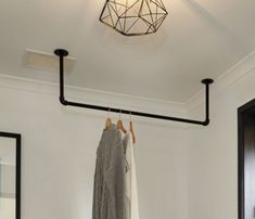 clothes hanging on rail in white room with black door and light fixture over bed area