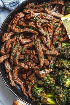 steak and broccoli in a skillet with lemon wedges on the side