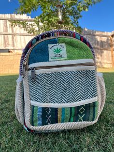 a multicolored backpack sitting on top of grass in front of a tree and fence