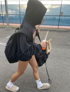 a person in a hoodie walking with a dog on a leash and holding a backpack