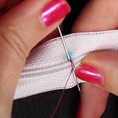 a woman's hands with pink nail polish holding a piece of fabric and thread