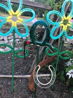 three metal garden stakes with flowers painted green, yellow and blue in the shape of horseshoes