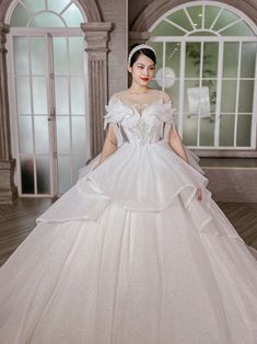 a woman in a white wedding dress standing on a wooden floor with windows behind her