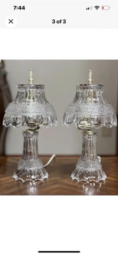 two clear glass lamps sitting on top of a wooden table next to a lamp shade