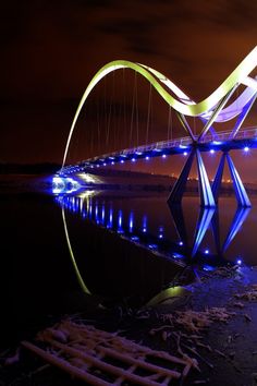 a bridge that is lit up at night with lights reflecting in the water below it