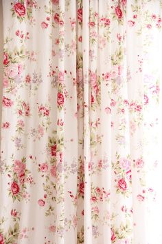 an open window with floral curtains hanging on the side and one curtain pulled down to reveal a pink flowered pattern