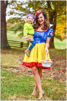 a woman holding a baby in her arms while wearing a snow white costume with red and yellow trim