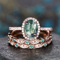 two wedding rings with an oval green stone surrounded by diamonds and emeralds on a rock