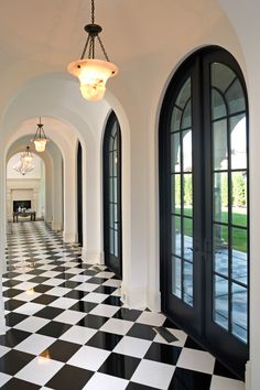 a hallway with black and white checkered flooring, arched doors and chandelier