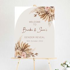 a welcome sign with flowers on it in front of a white wall and wooden easel