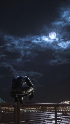 a man sitting on top of a bench next to a fence under a full moon