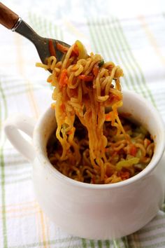 a spoon full of noodles is being lifted from a white bowl on a green and white checkered tablecloth