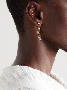 Gucci's gold-tone earrings feature a script version of the house's logo suspended from barbell-inspired posts. Wear yours as part of a stack with dainty studs. Designer Yellow Gold Jewelry With Logo Lettering, Gucci Luxury Drop Earrings, Classic Gucci Earrings For Anniversary, Gucci White Gold Sterling Silver Earrings, Gucci Luxury Sterling Silver Earrings, Luxury Gucci Sterling Silver Earrings, Gucci Sterling Silver Earrings As Gift, Gucci Sterling Silver Earrings For Gift, Elegant Gucci Sterling Silver Earrings