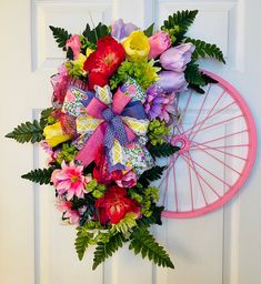 a pink bicycle wheel with flowers on the front door and a wreath hanging from it's side