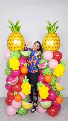 a woman standing in front of a giant balloon arch with fruit on it and pineapples