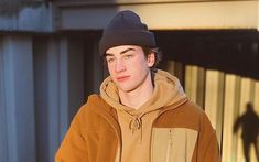 a young man in a brown hoodie holding a skateboard