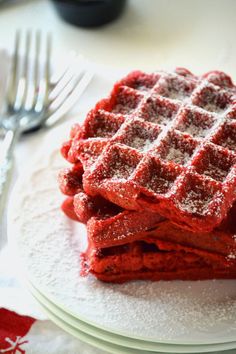 some red waffles on a white plate with fork and knife in the background