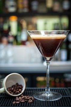 a martini glass filled with liquid next to coffee beans and a cup on a bar