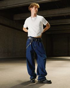 a young man in white shirt and jeans standing with his hands on his hips while looking at the camera