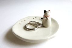 two wedding rings sitting on top of a white plate with a cat figurine