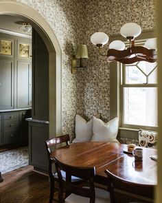 a dining room table and chairs in front of a window with an archway leading into the kitchen