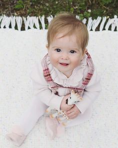 a baby sitting on top of a blanket holding a stuffed animal in her hands and smiling at the camera