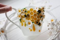 a coffee cup with bees and daisies on it is being held by a hand