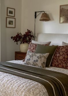 a bed with pillows and blankets on top of it next to a wall mounted lamp