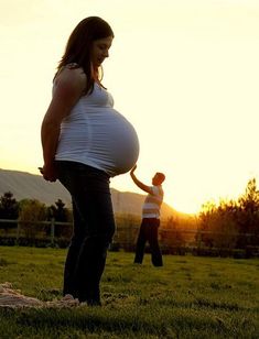 a pregnant woman standing on top of a lush green field