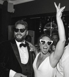 a man and woman wearing heart shaped sunglasses at a party with their arms in the air