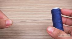 two hands holding a thread and needle on a wooden surface