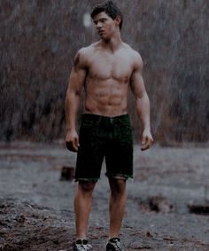 a shirtless man standing in the rain with his hands on his hips while wearing shorts