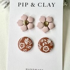 two pairs of pink and brown flower studs on a white card next to some flowers