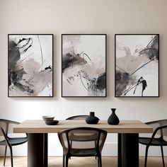 three black and white paintings hang above a dining room table