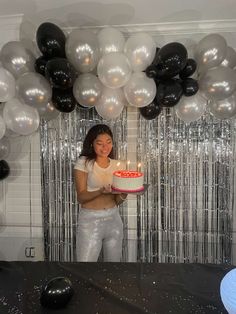 a woman holding a cake with candles in front of balloons