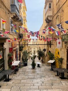 an alley way with tables and flags hanging from the buildings