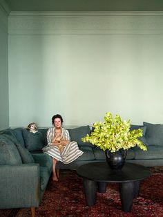 a woman sitting on a couch in front of a coffee table with a vase full of flowers