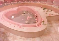 a heart shaped bathtub filled with water and pink flowers on the floor next to a tiled wall