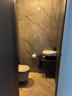 a bathroom with marble walls and flooring next to a white toilet sitting on top of a hard wood floor