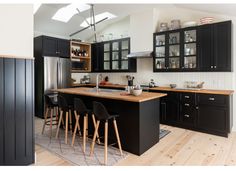 a kitchen with black cabinets and wooden floors is pictured in this image, there are four bar stools at the center of the island