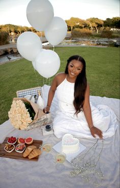 a woman sitting on top of a blanket next to white balloons and cake in front of her