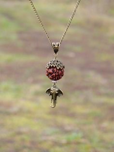 a necklace with an elephant head hanging from it's side and a red beaded ball on the end