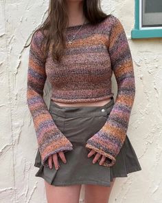 a woman standing in front of a white wall wearing a sweater and miniskirt